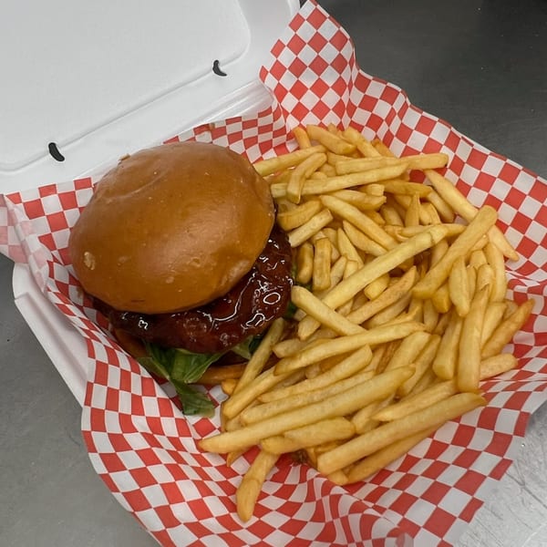 A burger with dark sauce and lettuce, alongside golden fries, in a red and white checkered paper-lined container.