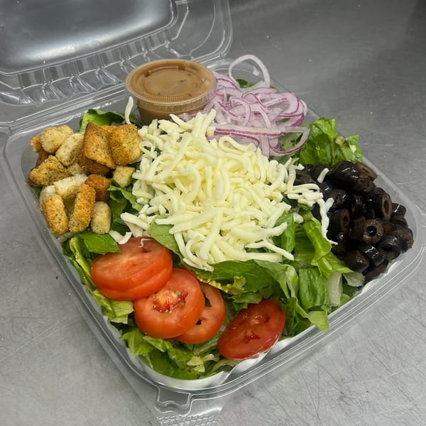 A Mia Ava East Coast Pizza side salad with lettuce, tomatoes, olives, cheese, onions, croutons, and dressing.