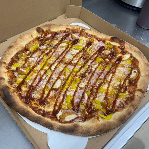 Mia Ava's BBQ chicken pizza with red onions, yellow peppers, and a BBQ sauce drizzle in a box.
