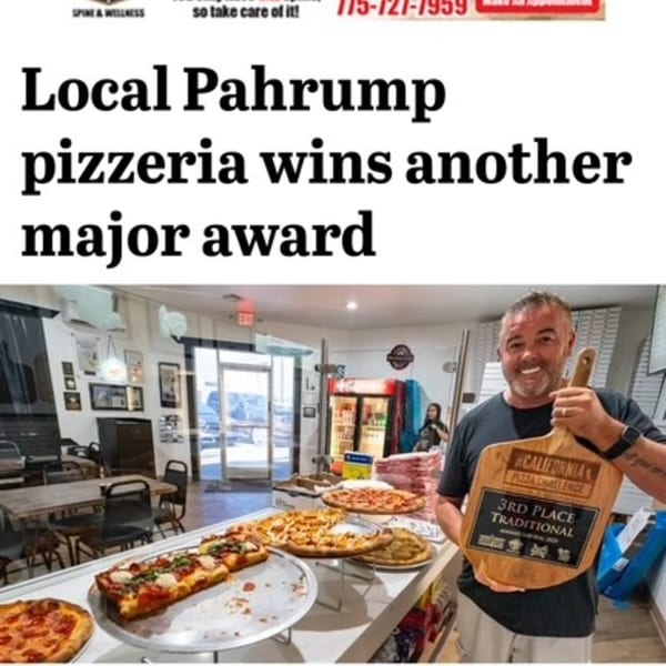 A smiling man holds a "3rd Place Traditional" award in a pizzeria with various pizzas on display.
